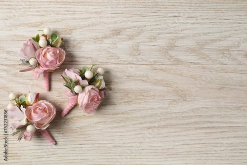 Stylish pink boutonnieres on white wooden table, flat lay. Space for text