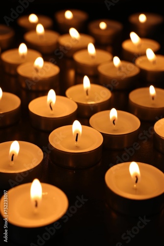 Burning tealight candles on dark surface  closeup