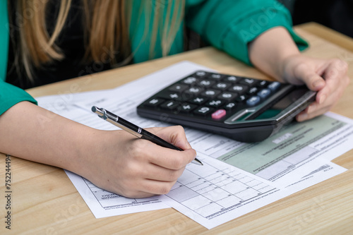 Kobieta siedzi przy biurku, wypełnia deklarację podatkowa i liczy na kalkulatorze  © Paweł Kacperek