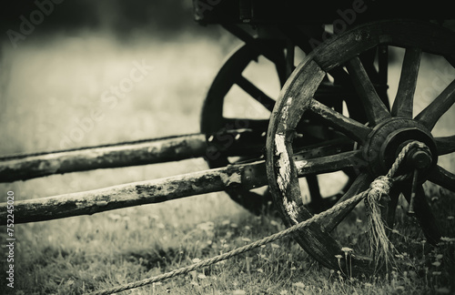 Monochrome photo of an old wooden cart with a sepia filter, which is typically pulled by horses, standing in the field. Agriculture and vintage transportation. Retro style.