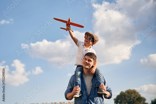 With aviator glasses, playing with toy plane. Father and little son are having fun outdoors
