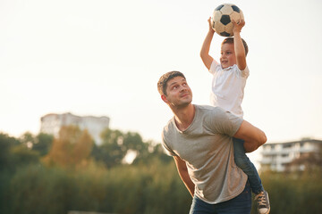 Holding professional soccer ball. Father and little son are playing and having fun outdoors