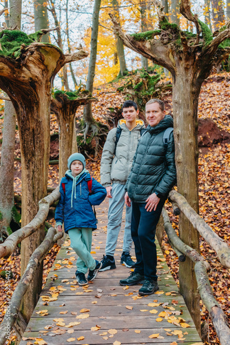 Wallpaper Mural dad and 2 sons in the autumn forest stand on the bridge. Happy family enjoy the spending vacation together in the nature. father and son hug in the wooden pier at the background river and fall leaves Torontodigital.ca