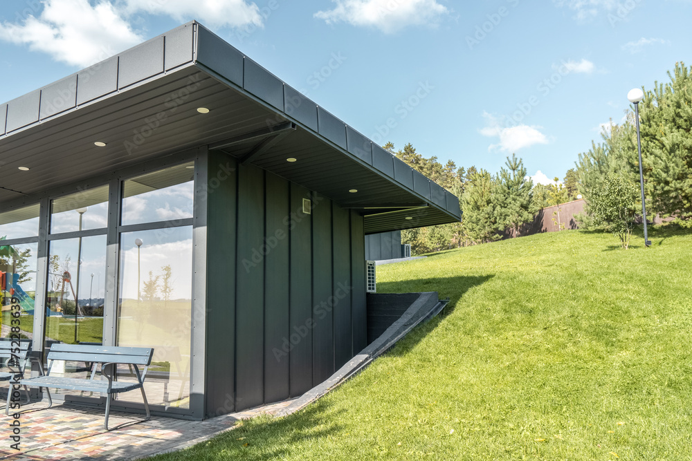 Modern guest house with standing seam facade panoramic glazing and large flat roof overhang in park. Minimalist architectural style of public building Modern guest house with standing seam facade panoramic glazing and large flat roof overhang in park. Minimalist architectural style of public building