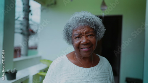 Obraz na plátně One joyful black elderly 80s woman with gray hair smiling at camera standing at humble domestic residence in South America