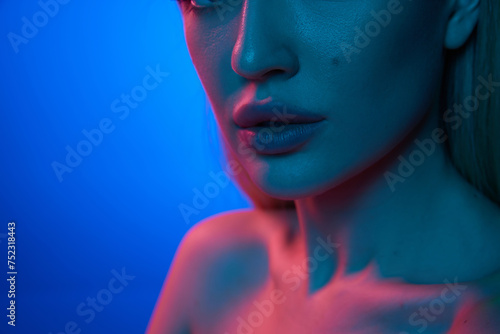 Cropped close-up image of beautiful female plump lips against blue studio background in neon light. Lip augmentation. Concept of natural beauty, cosmetology, cosmetics, skin care and health