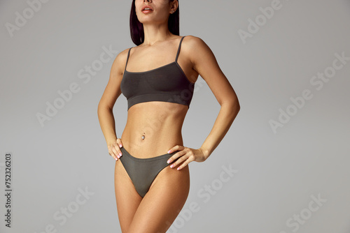 Cropped portrait of young female model in underwear posing holds hands on hips against grey studio background. Concept of beauty, spa procedures, dermatology treatments, cosmetology care.