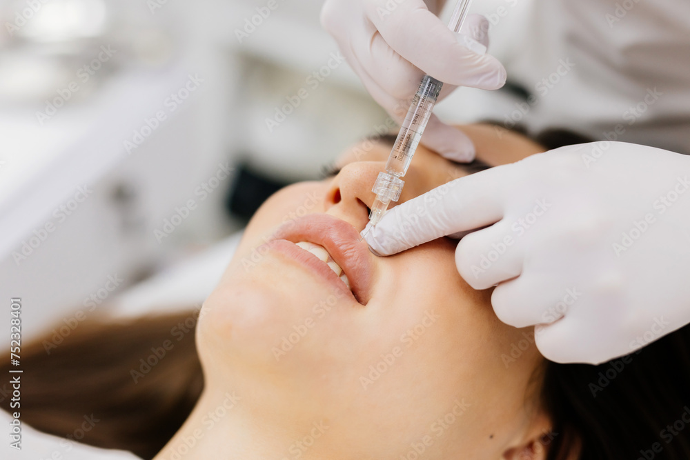 The procedure for lip augmentation and correction in a cosmetology salon. The specialist gives an injection to the patient's lips. Concept of cosmetology, cosmetic injections, and cosmetic surgery. The procedure for lip augmentation and correction in a cosmetology salon. The specialist gives an injection to the patient's lips. Concept of cosmetology, cosmetic injections, and cosmetic surgery.