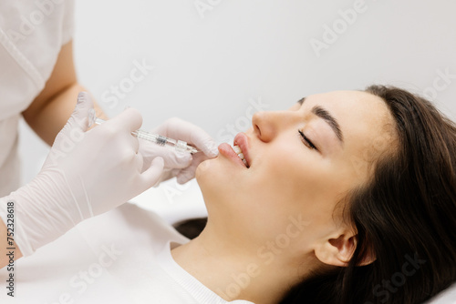 Injection lip augmentation. Close-up of beautician's hands doing cosmetic procedures for sexy female lips. Cosmetological treatment, cosmetic injections.