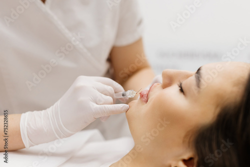 Injection lip augmentation. Close-up of beautician s hands doing cosmetic procedures for sexy female lips. Cosmetological treatment  cosmetic injections.