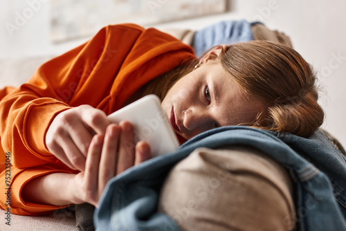 Billede på lærred troubled teenage girl using her smartphone and feeling down while lying on sofa
