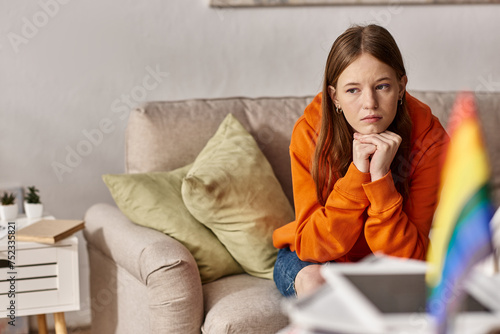 Photography Pensive teen girl in hoodie sits on couch with a distant look, blurred lgbtq fla