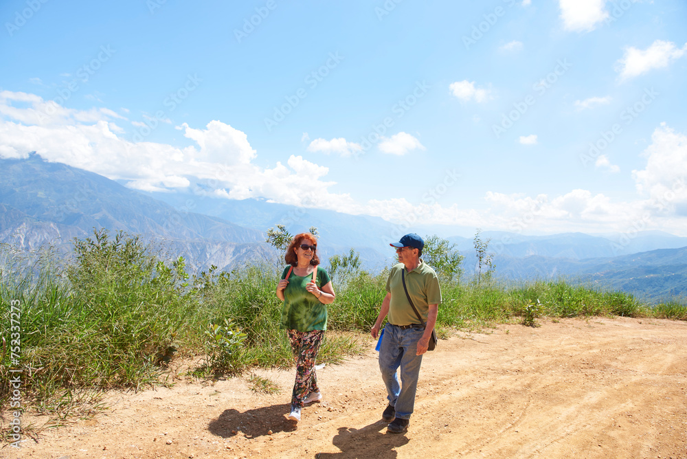 Hispanic senior hiking couple walking relaxed along a rural Andean road up a mountain in Santander, Colombia. Concept: active and healthy lifestyle after retirement.