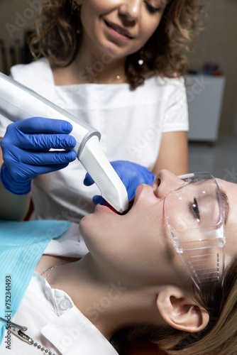 Orthodontist using a digital scanner to digitally capture the shape of blonde caucasian woman patient teeth gums for custom made invisible plastic aligners bracers. Quick oral scanning by the doctor