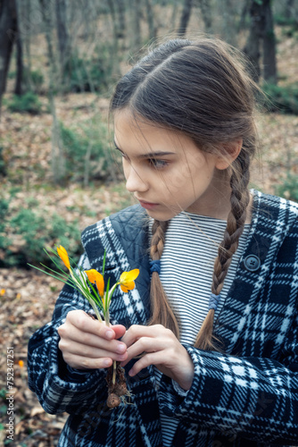 Beautiful caucasian girl with braids holding a bouquet of yellow crocuses at the background of a spring forest. © Jess_Ivanova