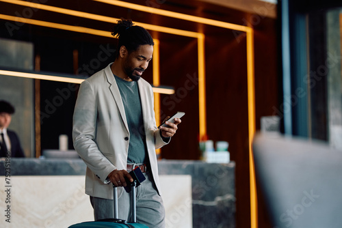 Happy black man using cell phone in hotel lobby. photo