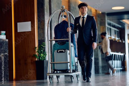 Happy bellboy pushing luggage cart with guest's suitcases in hotel. photo