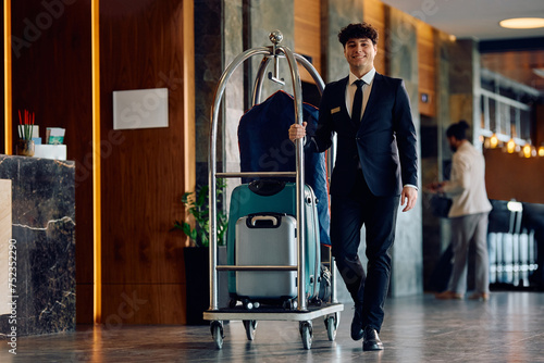 Fotografie Happy hotel attendant luggage cart through lobby and looking at camera