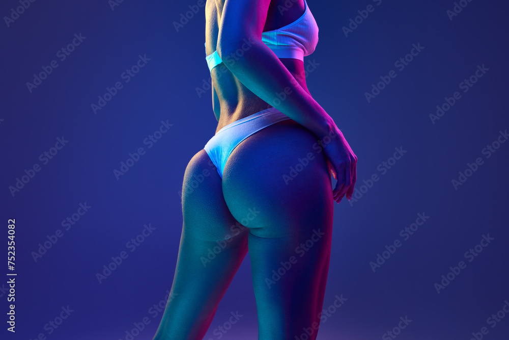 Cropped photo of perfect female body, buttocks in underwear in multicolored neon light against gradient blue studio background. Concept of beauty, spa procedures, dermatology treatments, cosmetology. - obrazy, fototapety, plakaty 