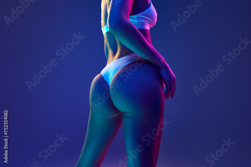 Cropped photo of perfect female body, buttocks in underwear in multicolored neon light against gradient blue studio background. Concept of beauty, spa procedures, dermatology treatments, cosmetology.