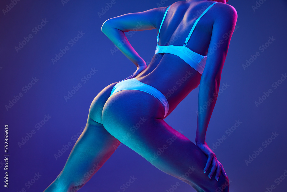 Cropped photo of young woman with slim body and smooth skin in multicolored neon light against gradient blue studio background. Concept of beauty, spa procedures, dermatology treatments, body care. - obrazy, fototapety, plakaty 