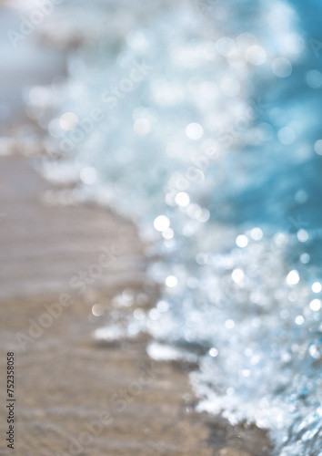Abstract blurred blue background of waves with splashes of sea or ocean on sandy beach on sunny summer day. Defocused water movement