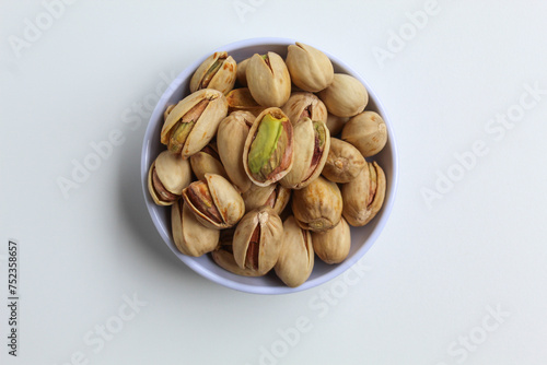 Salted pistachio on the small white bowl, isolated on white background, flat lay or top view