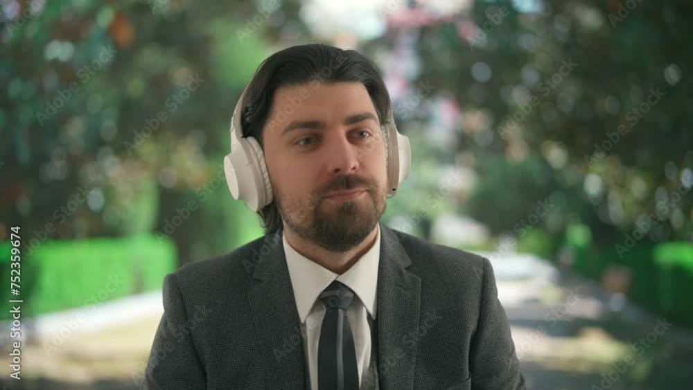 A young man enjoys music with large wireless headphones in the afternoon against the backdrop of a green park A young man enjoys music with large wireless headphones in the afternoon against the backdrop of a green park