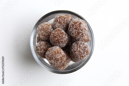 Tamarind ball candy in small glass. Sweet and sour candy made from tamarind paste and coated by sugar. Isolated on white background, flat lay or top view