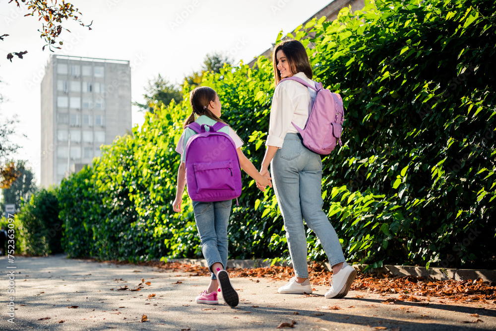 Obraz premium Full body rear behind photo of two charming sisters carry rucksack hold arms walk chatting sunshine park outside