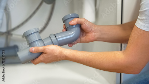 Close up of hands of plumber repairs plumbing pipes in kitchen sink. Replacement of plumbing pipes. Removing blockage clog in drain pipe. Sewerage