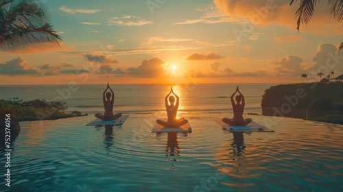 Three individuals practicing yoga during a serene sunrise by the ocean at a tranquil coastal resort.