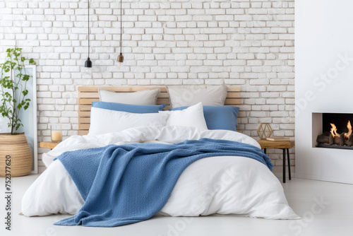 Bed with blue pillows and coverlet near fireplace against white brick wall Loft scandinavian interior design of modern bedroom photo