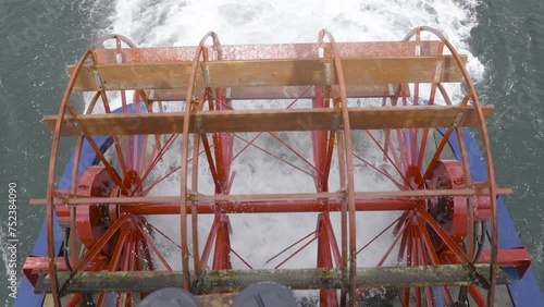 A 4k slow-motion video with a top-down view of a red paddle wheel on the back of a paddle boat.