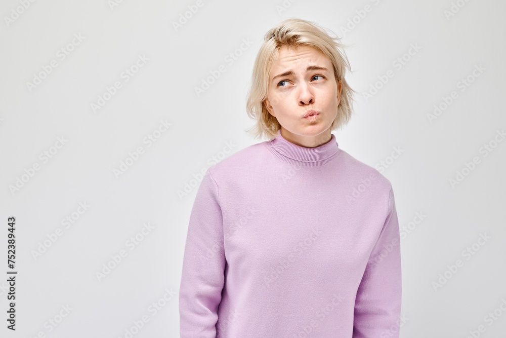 Confused young woman in a purple sweater, making a puzzled expression on a light gray background. Confused young woman in a purple sweater, making a puzzled expression on a light gray background.