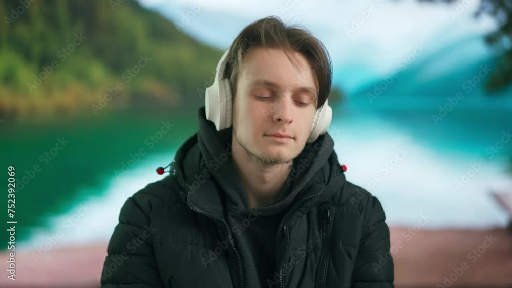 Young man enjoying music in large wireless headphones in the afternoon against a natural landscape. Young man enjoying music in large wireless headphones in the afternoon against a natural landscape.