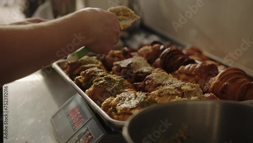 A baker prepares almond croissants by spreading almond paste on cut croissants.