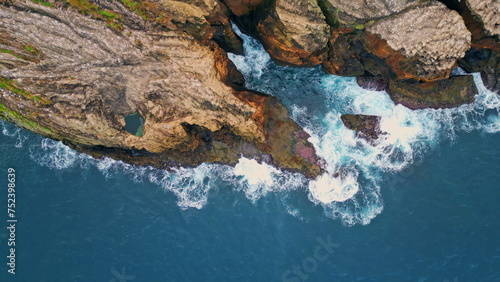 Foaming waves crashing rocky cliffs top view. Drone shot of dramatic coastline
