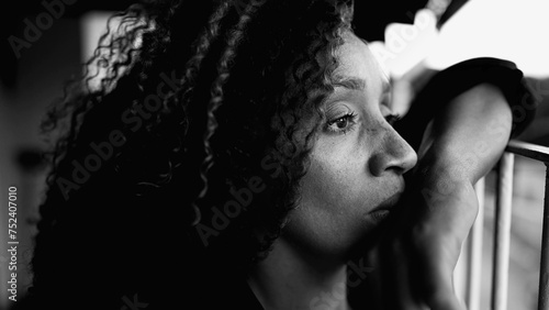 Sad Depressed 50s woman leaning on metal bar at home balcony feeling lost in thought in deeo mental rumination in intense dramatic black and white. Portrait of contemplative South American latina