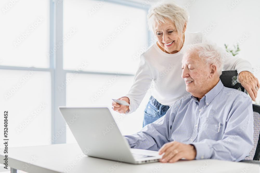 senior couple using a laptop while sitting at the office using credit card