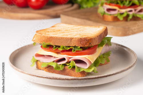 Close-up of two sandwiches with bacon, salami, prosciutto and fresh vegetables on rustic wooden cutting board. Club sandwich concept