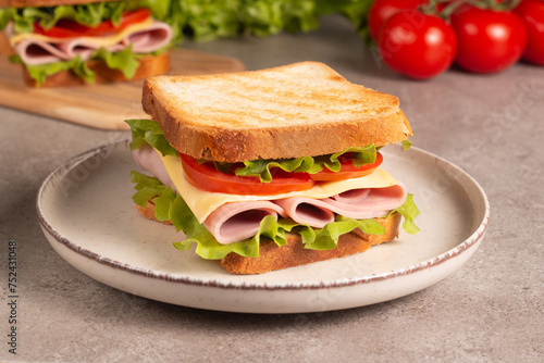 Close-up of two sandwiches with bacon, salami, prosciutto and fresh vegetables on rustic wooden cutting board. Club sandwich concept