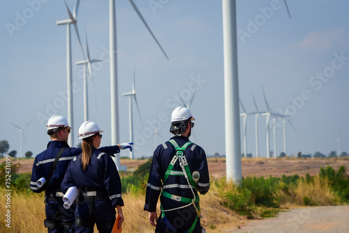 male and female electrical engineers and technicians wearing safety uniform workwear working outdoor, look at work site and discuss on a wind farm or wind turbines field used to produce electricity.