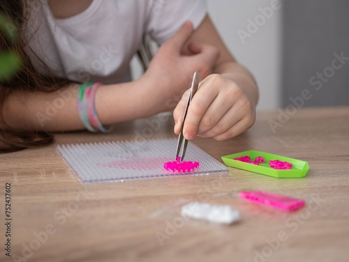 A close-up of a little girl's hand holding tweezers and assembling a toy from plastic parts of a thermo mosaic. The first stage of the work. Sensory education, hot plastic design.