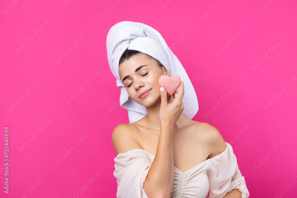 Beautiful cheerful attractive girl with a towel on her head, holds a sponge in the form of a pink heart. Beautiful cheerful attractive girl with a towel on her head, holds a sponge in the form of a pink heart.