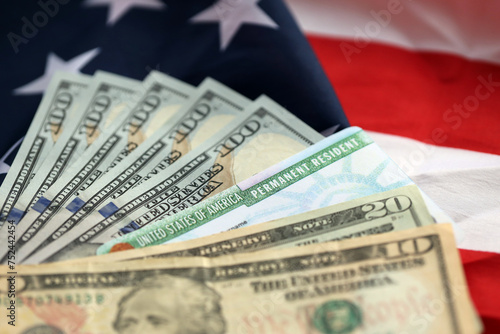 Permanent Resident United States of America Green Card and dollar bills on folded US flag close up photo