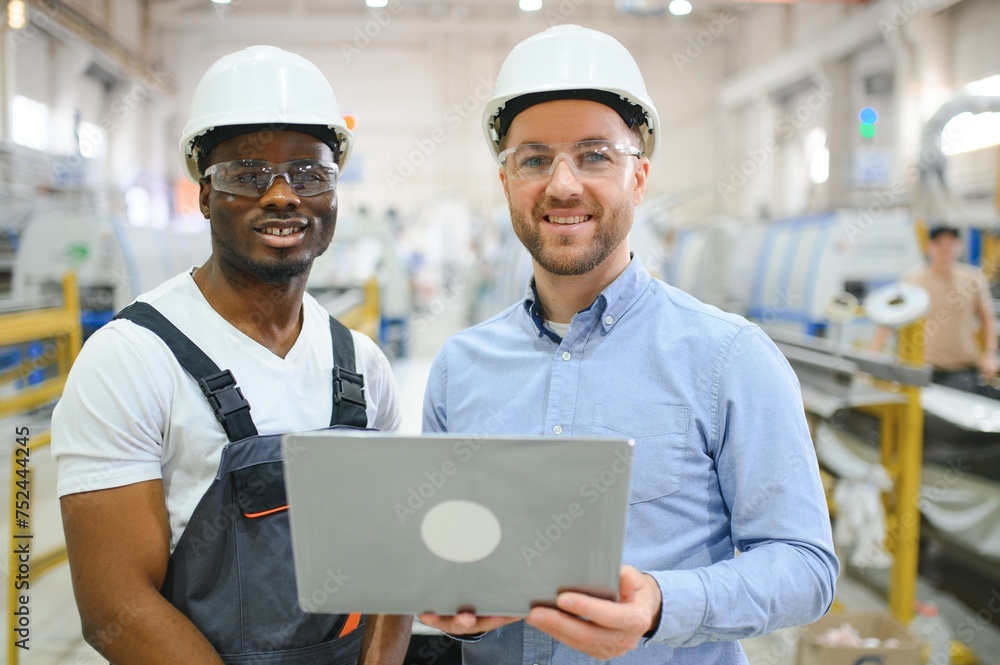 Two Diverse Professional Heavy Industry Engineers Wearing Safety Uniform and Hard Hats Working on Laptop Two Diverse Professional Heavy Industry Engineers Wearing Safety Uniform and Hard Hats Working on Laptop