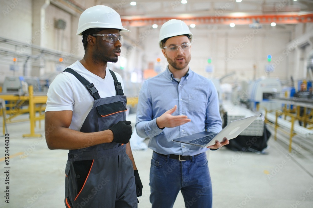 Two Diverse Professional Heavy Industry Engineers Wearing Safety Uniform and Hard Hats Working on Laptop Two Diverse Professional Heavy Industry Engineers Wearing Safety Uniform and Hard Hats Working on Laptop