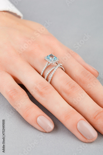 Beautiful female hand with gold ring with diamonds and aquamarine on gray background