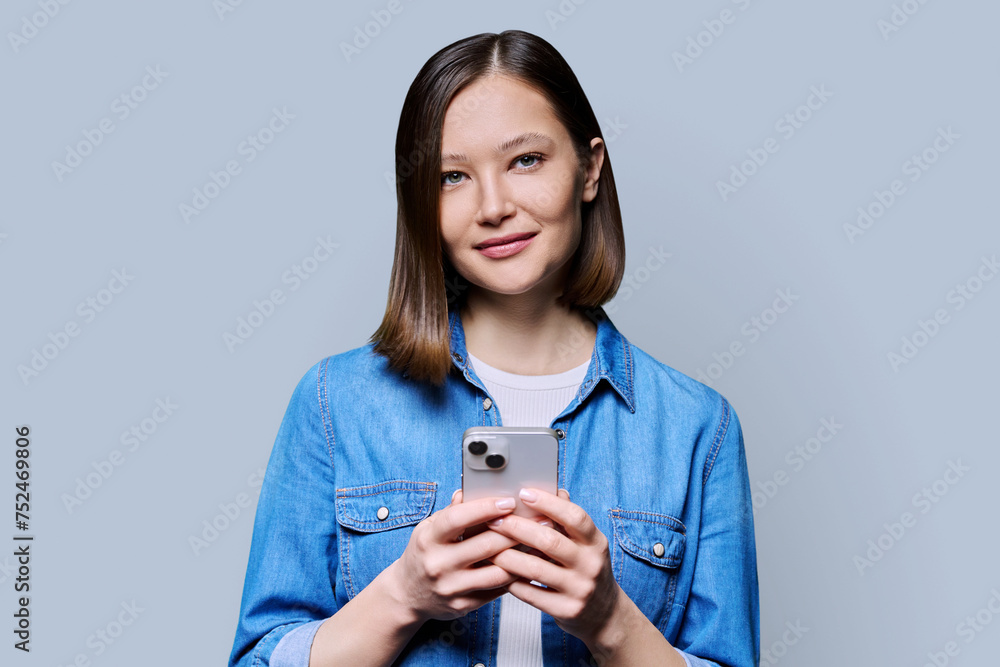 Young smiling woman using smartphone looking at camera in gray background
